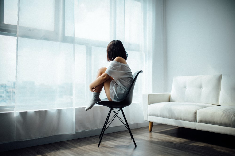 woman sitting in chair hugging legs and looking out window